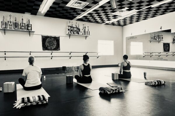 Black and white photo of a group of three doing yoga in a studio.